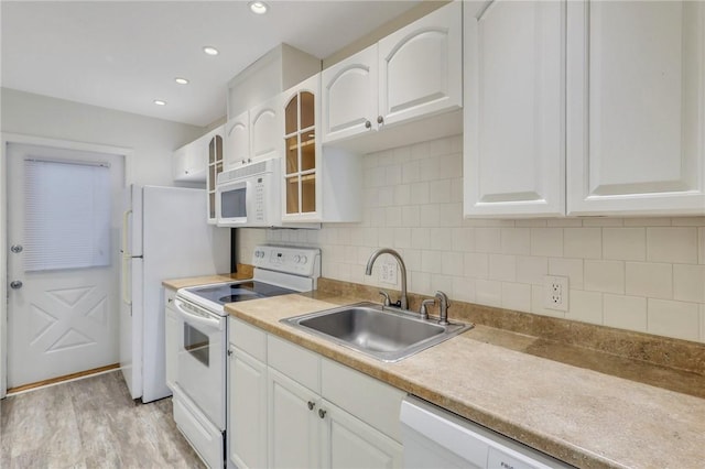 kitchen featuring white cabinetry, sink, backsplash, light hardwood / wood-style floors, and white appliances