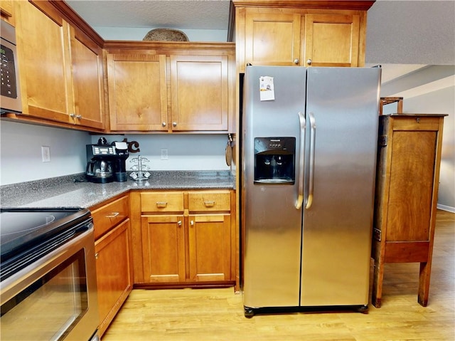 2300 Albany Ave, Waycross, GA 31503 - kitchen with appliances with stainless steel finishes, light wood-type flooring, brown cabinetry, and dark stone countertops