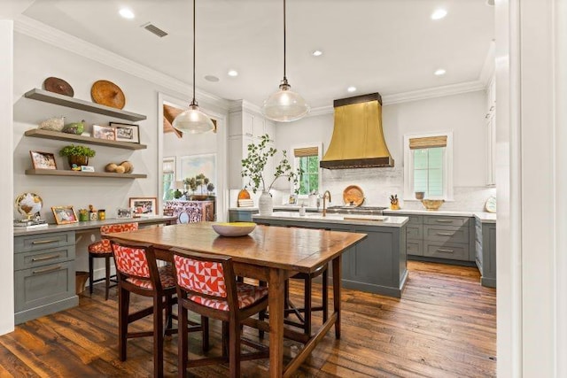 kitchen featuring gray cabinetry, hanging light fixtures, dark hardwood / wood-style floors, custom range hood, and ornamental molding