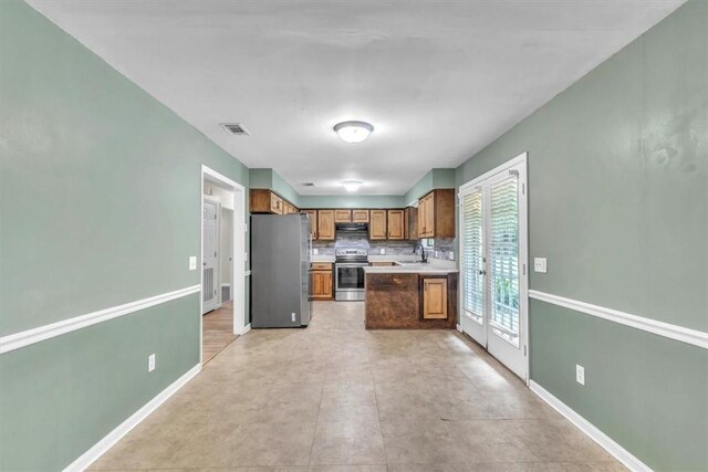 122 Tyson Ln, Allenhurst, GA 31301 - kitchen featuring appliances with stainless steel finishes, brown cabinetry, decorative backsplash, range hood, and light countertops