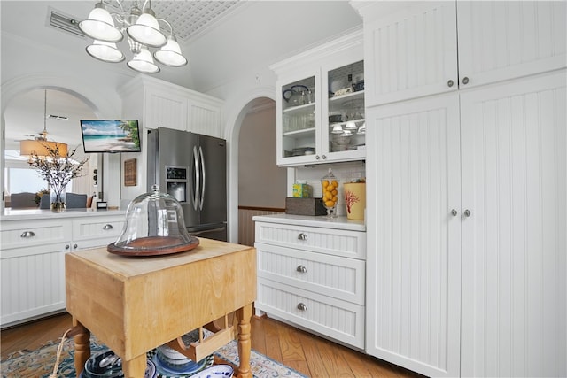 kitchen with stainless steel fridge, a chandelier, arched walkways, wood finished floors, and glass insert cabinets