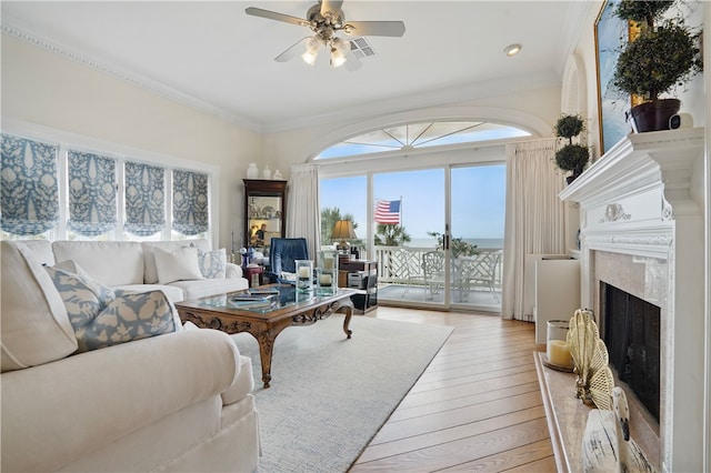 living area featuring crown molding, a high end fireplace, light wood-style floors, and a ceiling fan