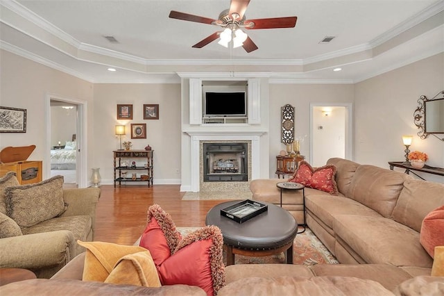 living room featuring ceiling fan, a large fireplace, hardwood / wood-style floors, a tray ceiling, and ornamental molding