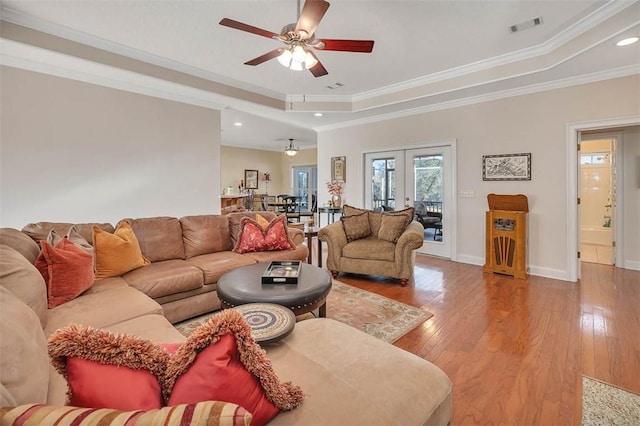 living room with a raised ceiling, ceiling fan, and ornamental molding