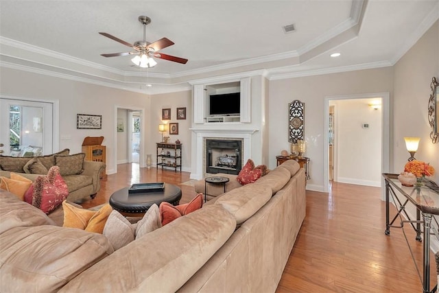 living room featuring ceiling fan, a raised ceiling, crown molding, and light hardwood / wood-style flooring