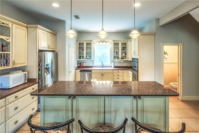 kitchen with appliances with stainless steel finishes, sink, dark stone countertops, a center island, and hanging light fixtures