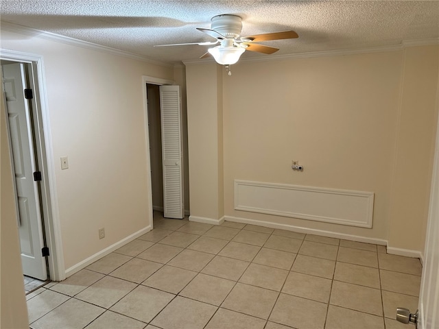 unfurnished room featuring ornamental molding, a ceiling fan, light tile patterned flooring, a textured ceiling, and baseboards