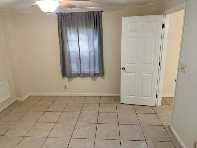 empty room with light tile patterned floors, ceiling fan, baseboards, and crown molding