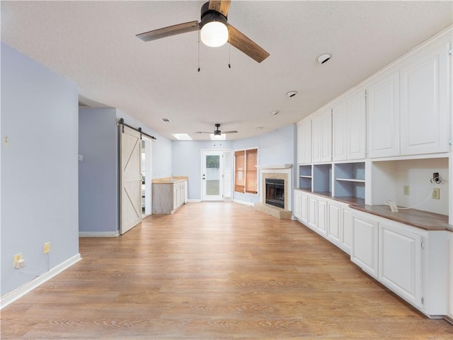 unfurnished living room with light wood-type flooring, ceiling fan, and a barn door