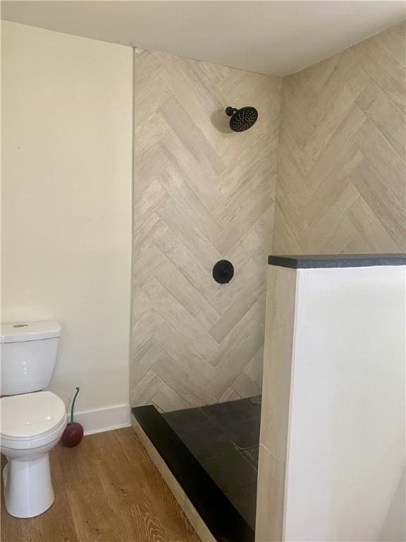 bathroom with tiled shower, toilet, and hardwood / wood-style flooring