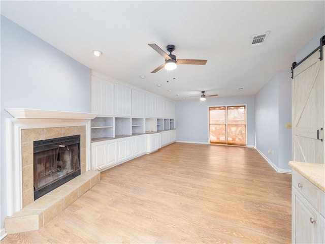 unfurnished living room with light wood-type flooring, ceiling fan, a barn door, and a fireplace