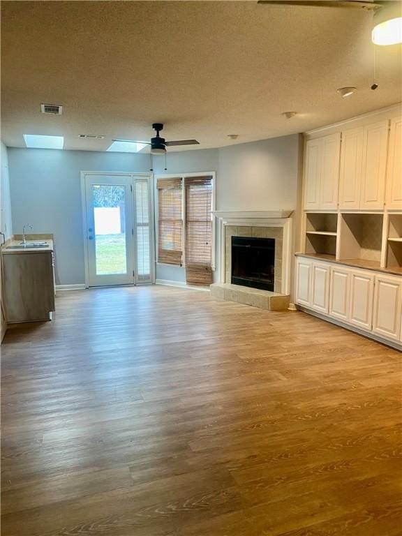 unfurnished living room featuring a textured ceiling, ceiling fan, sink, light hardwood / wood-style floors, and a tiled fireplace