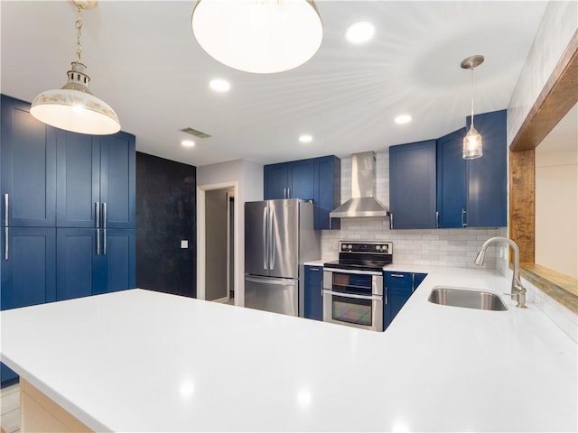 kitchen with wall chimney exhaust hood, stainless steel appliances, blue cabinetry, pendant lighting, and sink