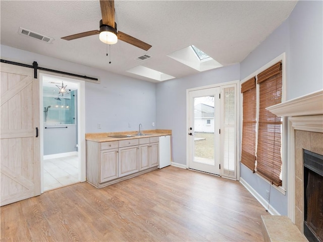 kitchen featuring white dishwasher, a tiled fireplace, light hardwood / wood-style floors, a barn door, and sink