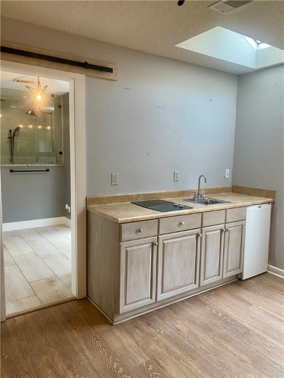 kitchen with dishwasher, black electric stovetop, sink, light hardwood / wood-style flooring, and a textured ceiling