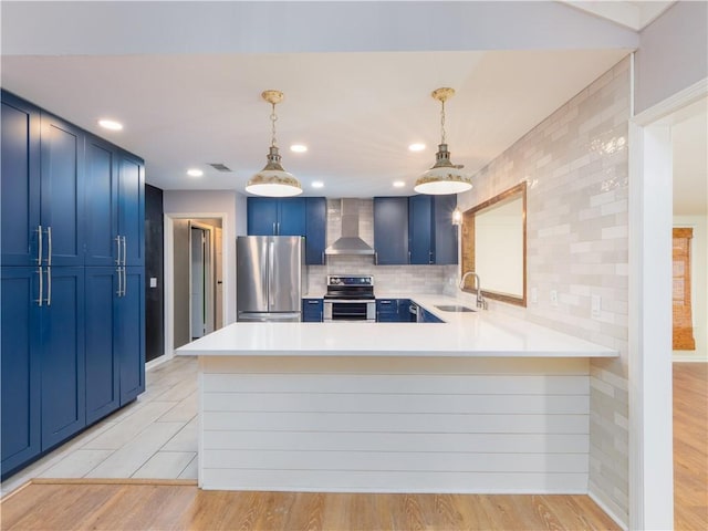 kitchen with kitchen peninsula, appliances with stainless steel finishes, wall chimney exhaust hood, and pendant lighting