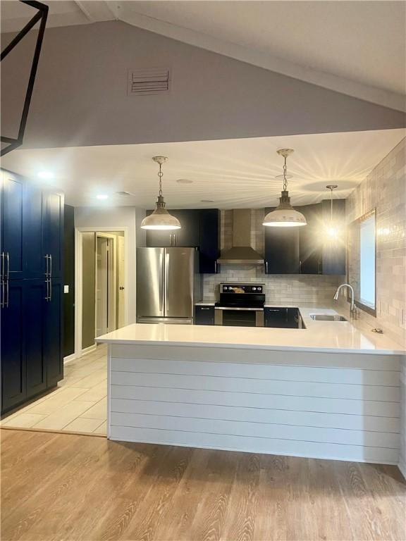 kitchen with sink, wall chimney exhaust hood, stainless steel appliances, and decorative light fixtures