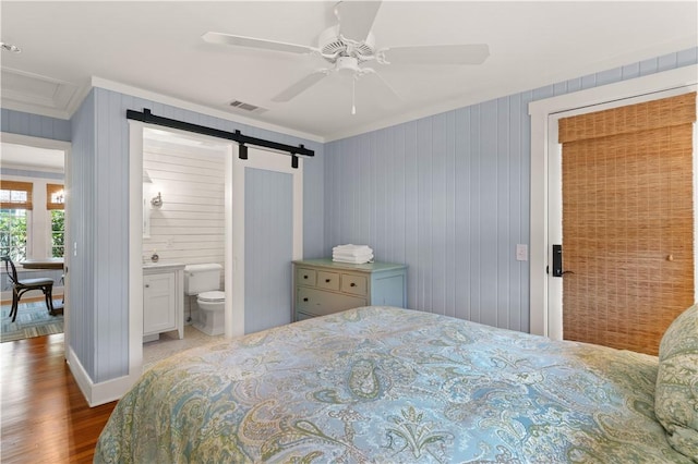 bedroom featuring crown molding, ensuite bath, ceiling fan, a barn door, and dark hardwood / wood-style floors