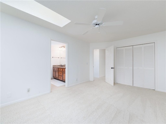 unfurnished bedroom with ensuite bathroom, a closet, carpet, a skylight, and baseboards