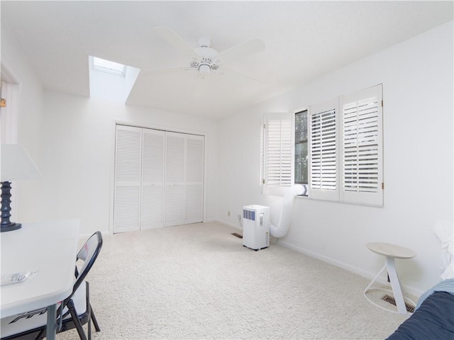 carpeted bedroom with a skylight, baseboards, a closet, and ceiling fan