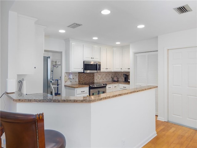 kitchen featuring visible vents, appliances with stainless steel finishes, white cabinetry, and a peninsula