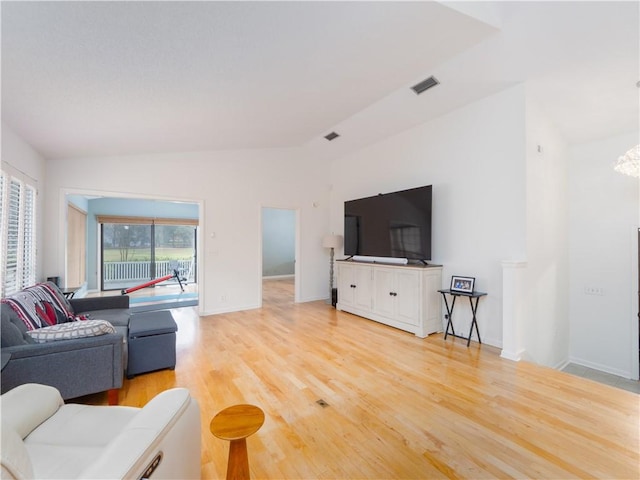 living area with visible vents, baseboards, light wood-style floors, and vaulted ceiling