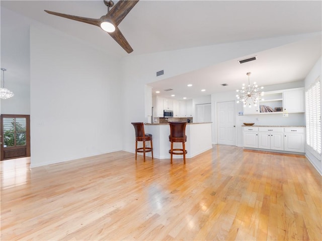 living room featuring high vaulted ceiling, ceiling fan with notable chandelier, visible vents, and light wood-type flooring