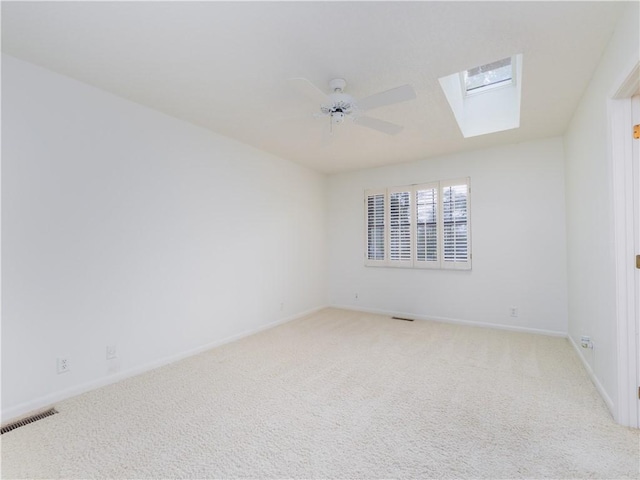 empty room with visible vents, a ceiling fan, a skylight, baseboards, and light colored carpet