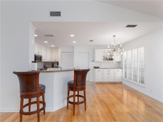 kitchen with stainless steel microwave, white cabinets, a breakfast bar area, and visible vents