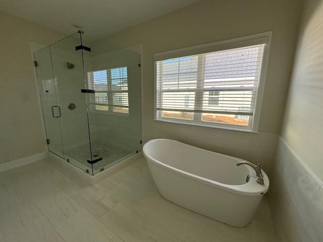 bathroom with a freestanding tub, a shower stall, baseboards, and a wealth of natural light