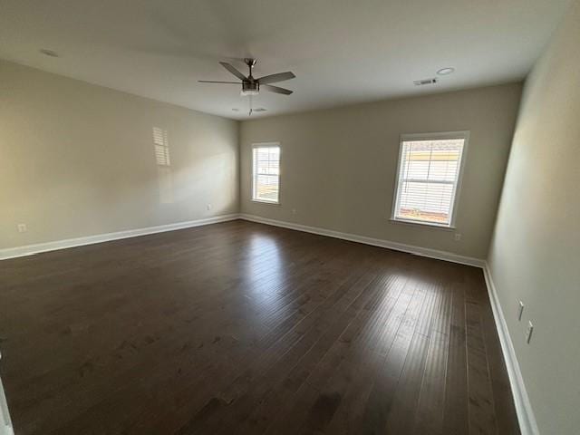 spare room with a ceiling fan, visible vents, baseboards, and dark wood-style flooring