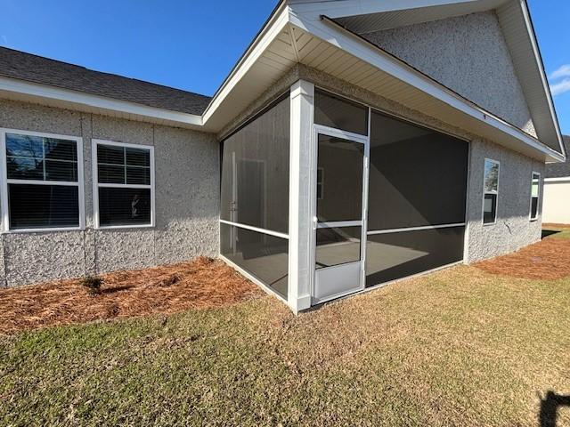 view of home's exterior with a sunroom, a lawn, and stucco siding