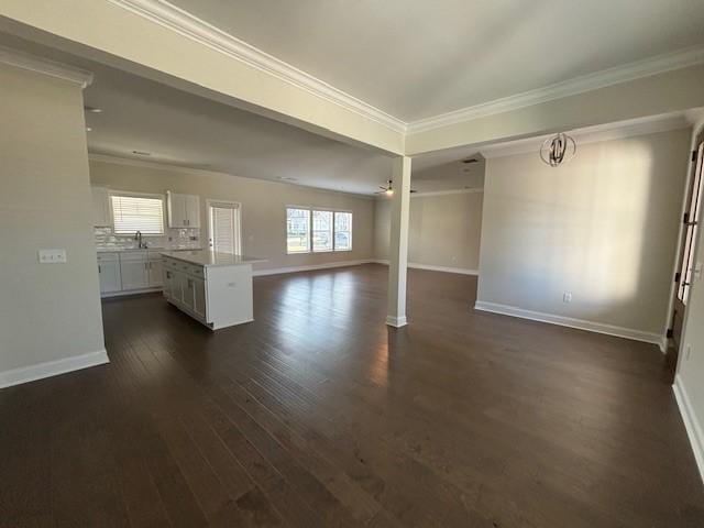 unfurnished living room with a sink, baseboards, ornamental molding, and dark wood-type flooring