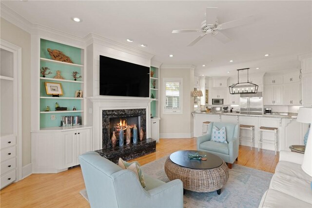 living room with crown molding, ceiling fan, light wood finished floors, a premium fireplace, and recessed lighting