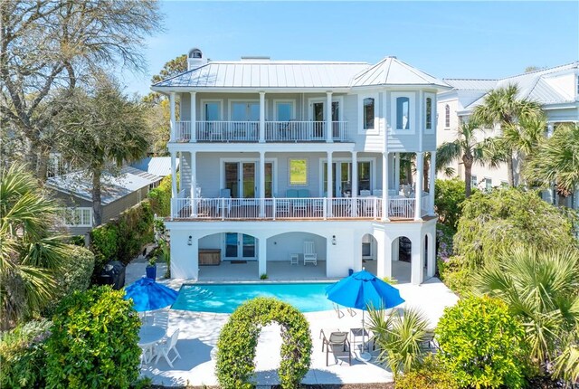 rear view of house with a balcony, an outdoor pool, a patio, metal roof, and a standing seam roof