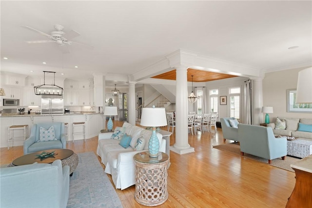 living room featuring recessed lighting, ceiling fan with notable chandelier, light wood-style flooring, and decorative columns