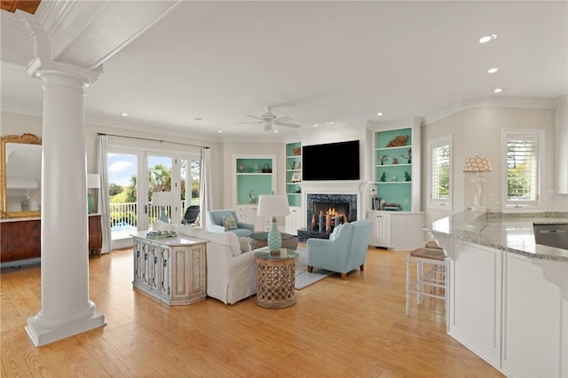 living area featuring recessed lighting, a warm lit fireplace, decorative columns, light wood-style flooring, and ceiling fan