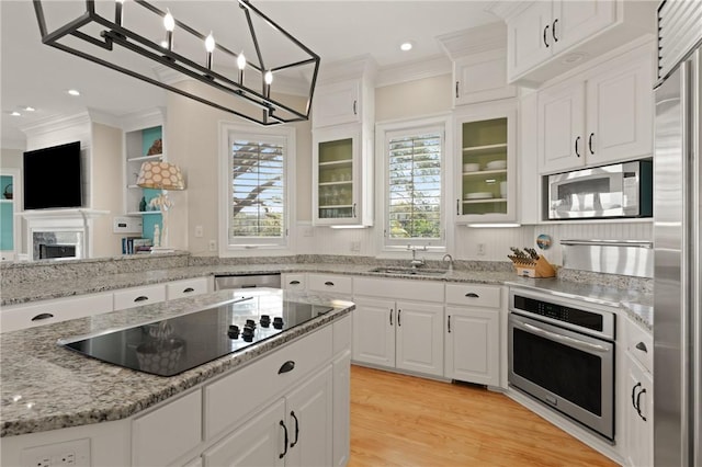 kitchen with white cabinetry, built in appliances, ornamental molding, and a sink