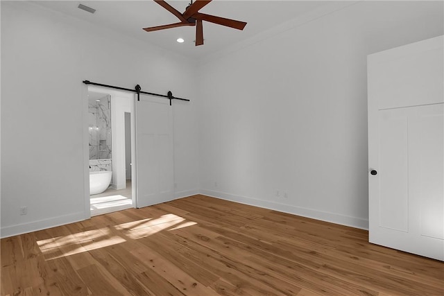 unfurnished bedroom featuring hardwood / wood-style floors, connected bathroom, ornamental molding, ceiling fan, and a barn door