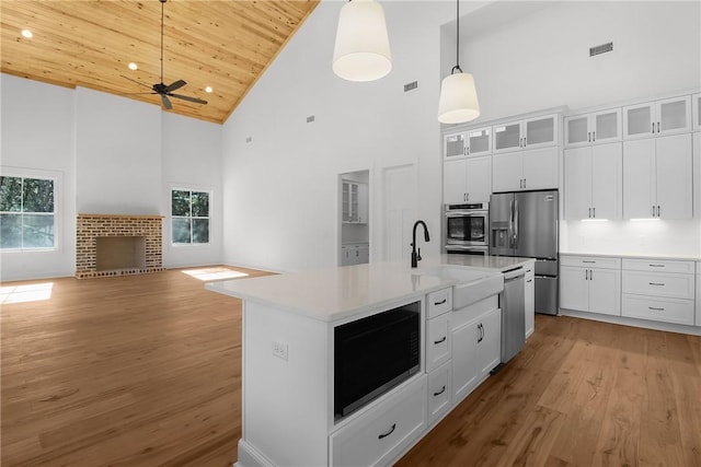 kitchen with appliances with stainless steel finishes, wood ceiling, white cabinetry, and a center island with sink