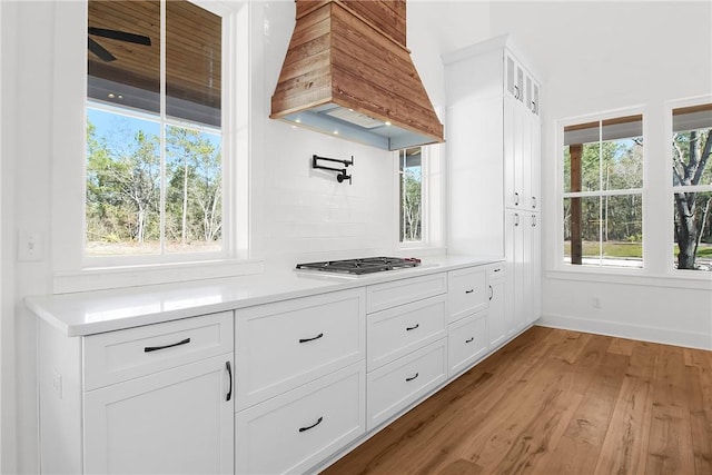 kitchen featuring stainless steel gas stovetop, premium range hood, white cabinetry, light hardwood / wood-style flooring, and plenty of natural light