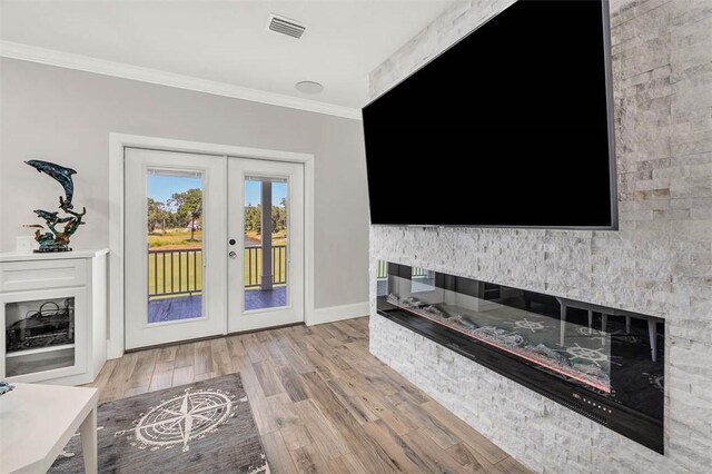 unfurnished living room featuring a stone fireplace, french doors, ornamental molding, and light wood-type flooring