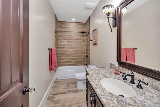 full bathroom featuring a textured ceiling, vanity, toilet, and tiled shower / bath