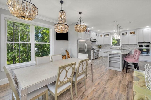 dining area with plenty of natural light, light hardwood / wood-style floors, ornamental molding, and a chandelier