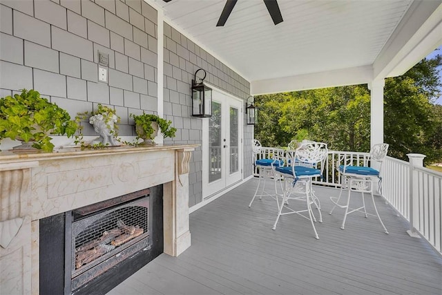 wooden terrace with a tiled fireplace, ceiling fan, french doors, and a porch