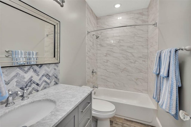 full bathroom featuring tiled shower / bath combo, hardwood / wood-style floors, toilet, decorative backsplash, and vanity