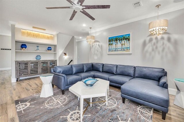 living room featuring hardwood / wood-style floors, ceiling fan with notable chandelier, built in shelves, and crown molding