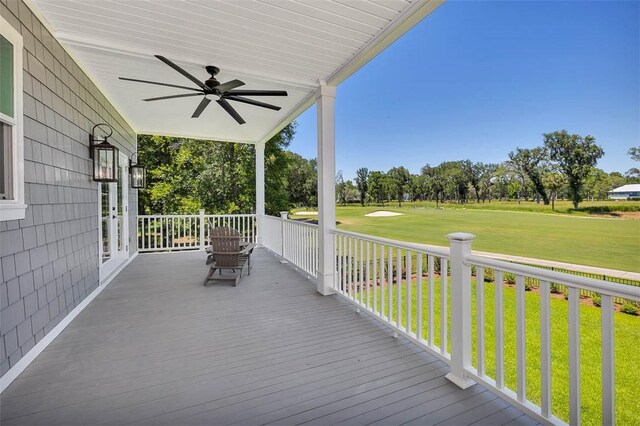 wooden terrace featuring a lawn, ceiling fan, and covered porch