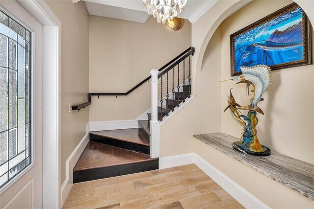 stairway with hardwood / wood-style floors, a healthy amount of sunlight, ornamental molding, and an inviting chandelier