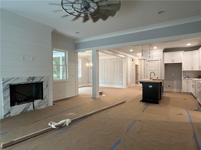 kitchen with pendant lighting, ceiling fan with notable chandelier, a fireplace, white cabinetry, and a center island with sink